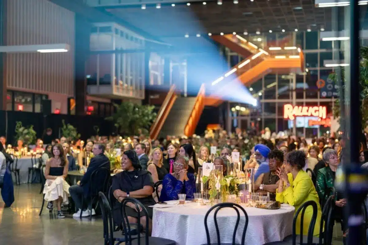 union-hall-1200×800 Guests seated at round tables during a formal banquet in a modern venue, with candles and a bright orange staircase in the background.